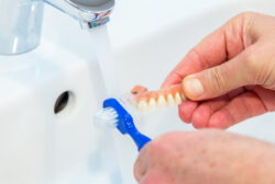 専用ブラシを使い入れ歯を流水で洗っているイメージ
